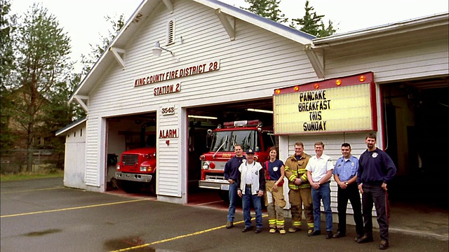 一群消防员站在消防站前，背景是消防车和闪烁的标志视频素材