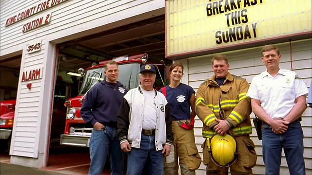 消防队员站在消防站前微笑，后面是消防车和指示牌视频下载