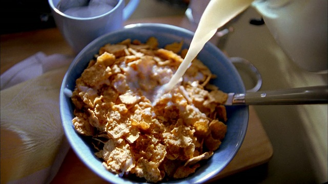 靠近在蓝色碗里的麦片，旁边有勺子和咖啡杯，牛奶倒进碗里视频下载