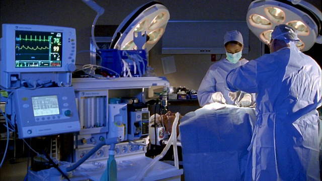 中镜头三名外科医生对病人进行腹部手术，前景中有医疗设备视频素材