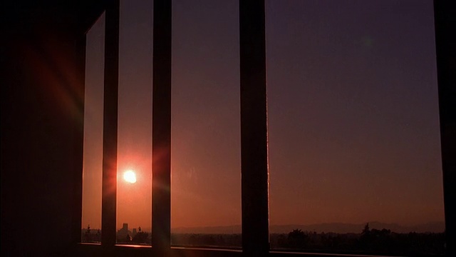 摄影车通过带有垂直百叶窗的办公室窗户拍摄日落时的橘色视频素材