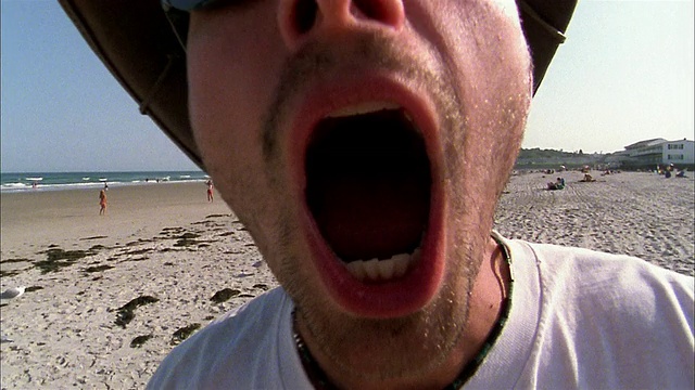 近距离的男人在太阳眼镜擦拭镜头w/毛巾和吹在海滩上的镜头视频下载
