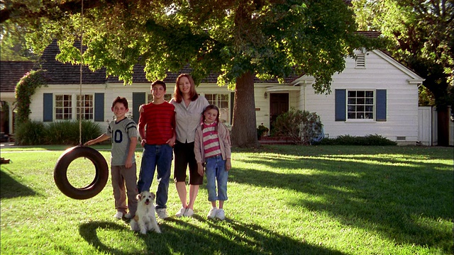 中镜头镜头缩小母亲与孩子和狗的轮胎秋千在前院郊区的房子视频素材