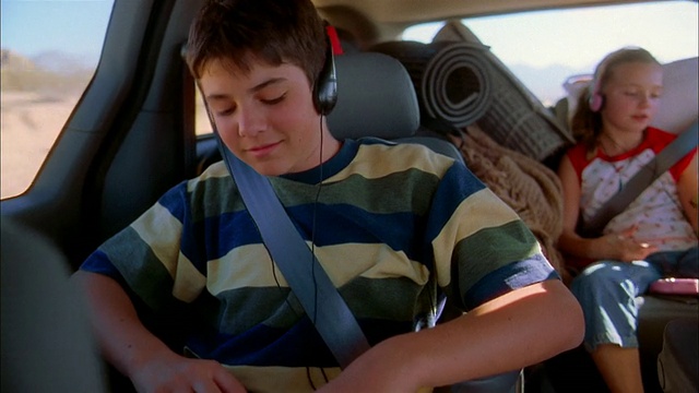 中等镜头的男孩坐在小货车里听音乐，带着耳机/把耳机递给弟弟视频素材