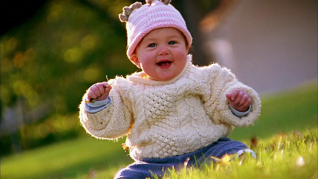 中拍婴儿在毛衣和针织帽坐+抱草户外视频素材