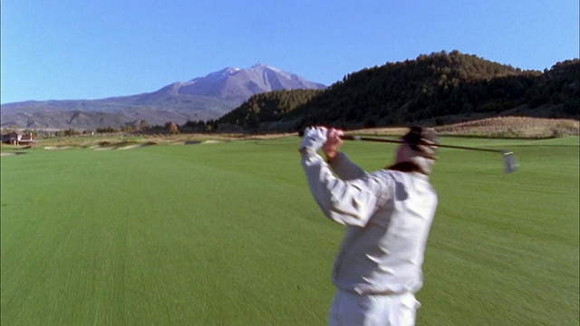 高角度摄影拍摄男性高尔夫球手击球驱动器高尔夫球场w/山在背景视频素材