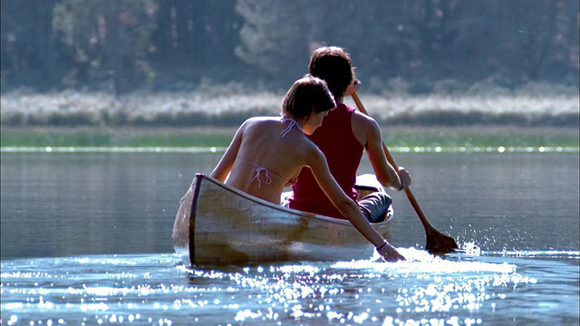 慢动作倾斜夫妇划着独木舟在湖上/女人的手舀水视频下载