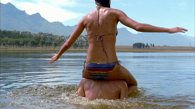中镜头的女人穿着比基尼骑在男人的肩膀上，在湖里旋转视频下载