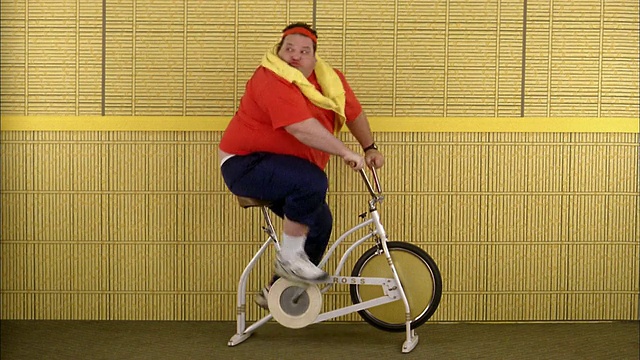 中等身材的胖子骑着健身自行车，看着身后视频素材