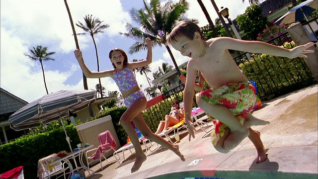 慢动作中镜头跟踪镜头小男孩和女孩跑步+跳进游泳池/微笑在CAM视频素材