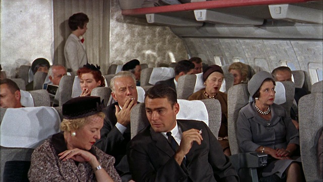 20世纪60年代，707飞机/空乘人员穿过过道时，中镜头乘客在聊天和吸烟视频素材
