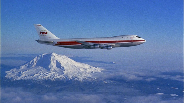 20世纪70年代的广角环球航空747喷气式飞机飞过云和雪山的背景视频下载