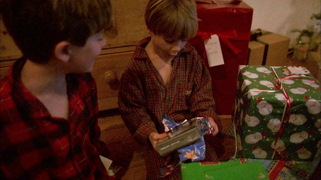 中镜头两个男孩打开圣诞礼物在客厅/男孩打开电子游戏和欢呼视频素材