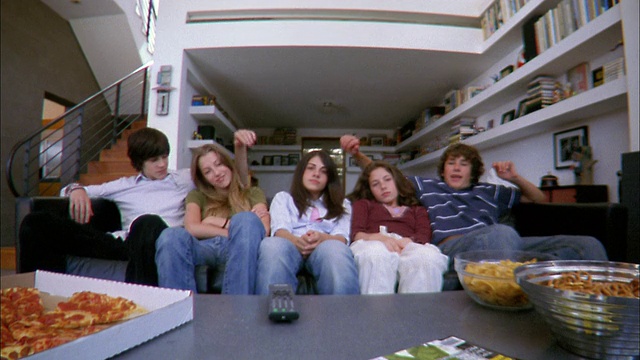低角度中镜头男孩把DVD放进播放器/五个青少年靠在客厅看视频视频下载