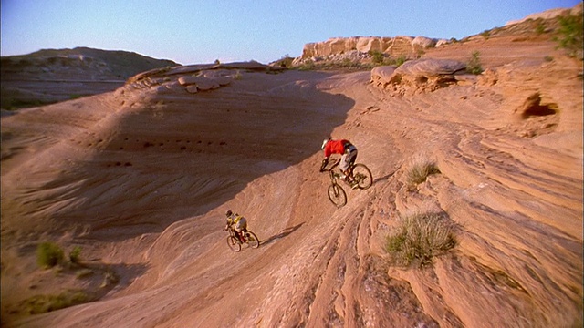 低角度中拍摄两名男子在山地车上跳跃/高角度骑下坡视频素材