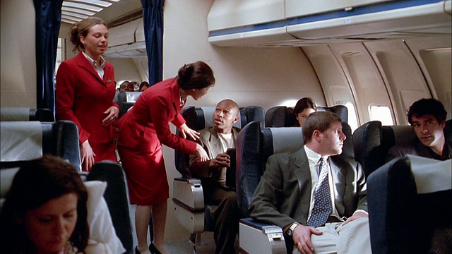 中镜头空乘人员在飞机上为乘客准备着陆/乘客抬高座椅靠背视频素材