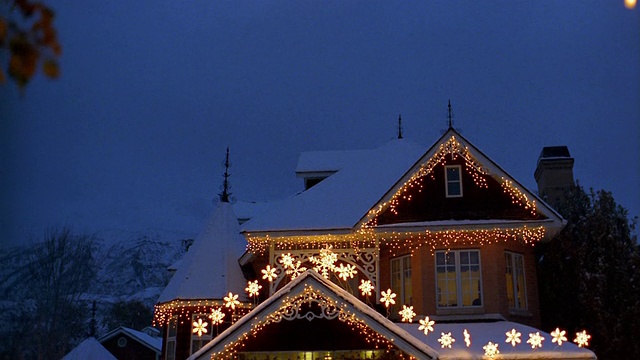 宽镜头倾斜下被白雪覆盖的房子装饰着圣诞灯/窗户灯出去视频素材