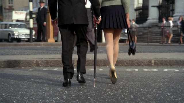 60年代低角度近距离拍摄穿迷你裙的女人等着过马路/带伞的男人和女人过马路视频下载