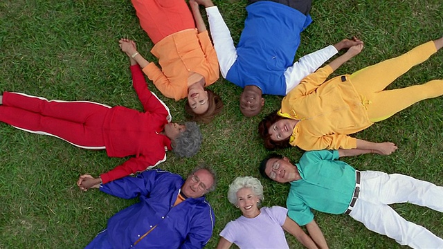 高角度中景拍摄一群老年人躺在草地上，手拉手围成一圈视频下载