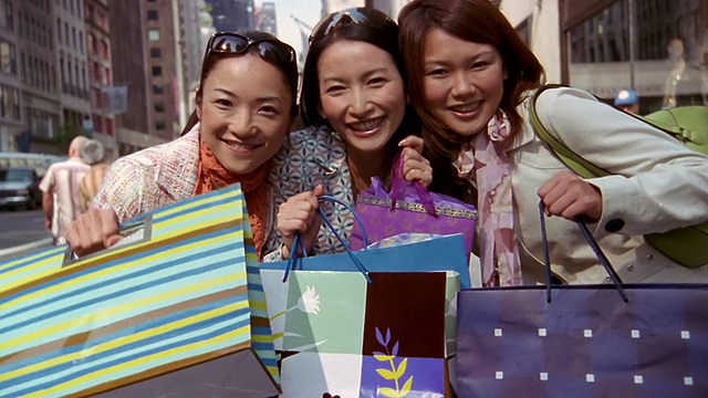 近距离倾斜两个女人微笑/缩小三个女人摆姿势与购物袋/纽约市视频素材