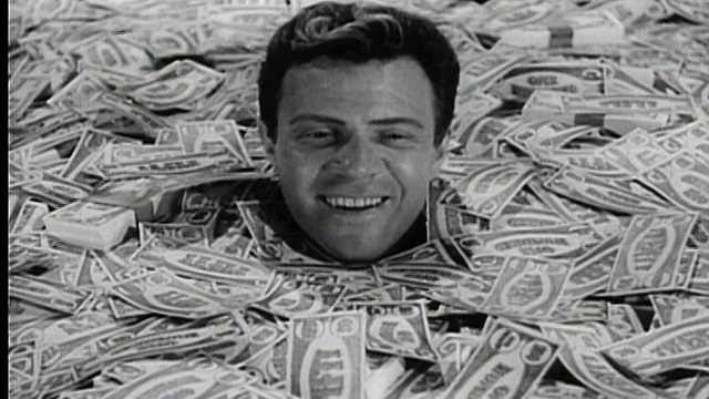20世纪60年代的黑人和白人埋在钱堆里微笑着抬头看着散落在他周围的钞票视频素材