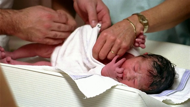 在比利时布鲁塞尔的医院里，一名中等照片的新生儿正在由父亲和助产士给他穿衣服视频素材