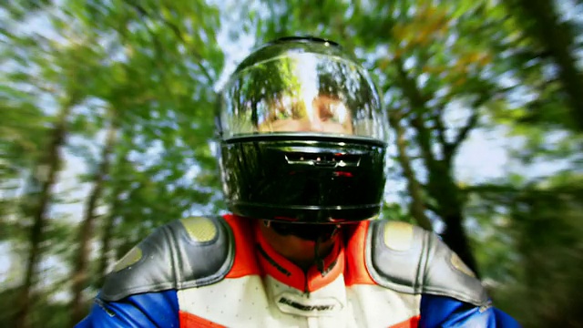 低角度近景男子戴摩托车头盔骑摩托车通过森林/布伦特伍德，埃塞克斯，英格兰视频下载