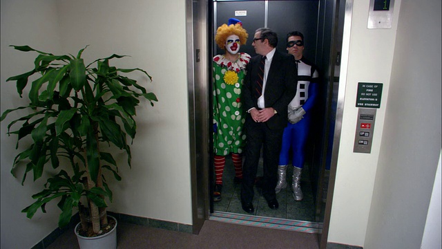(广角镜头)商人等电梯/和小丑和超级英雄一起进电梯/小丑大笑/低角度视频素材