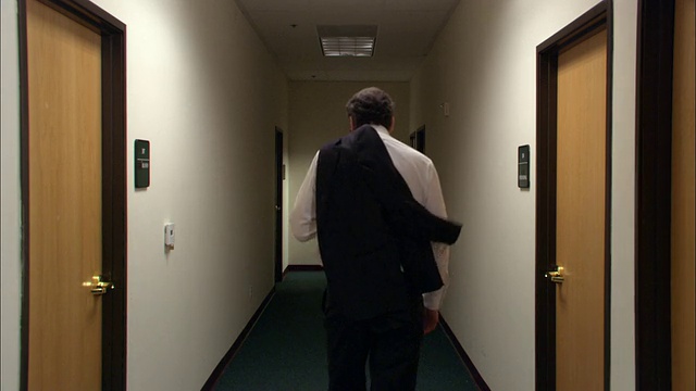 中等镜头的男性办公室职员将西装外套挎在肩上走下大厅/关灯/低角度视频素材