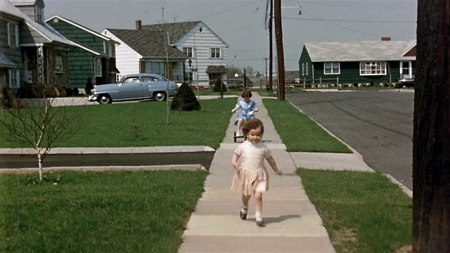 20世纪50年代，年轻女孩骑着三轮车在社区的人行道上跑向CAM视频下载