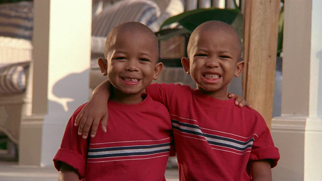 小双胞胎男孩的近距离肖像，穿着相配的衣服/在CAM微笑，看着对方/迈阿密视频素材