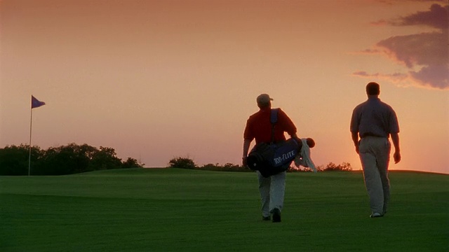 中等射击的高尔夫球手和球童在黄昏的高尔夫球场上行走/海湾港，密歇根视频素材