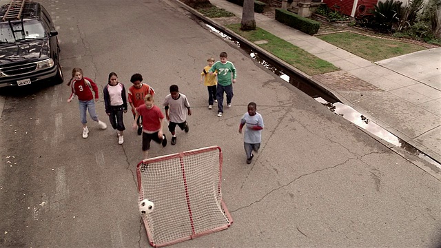 高角度广角射门在街上踢足球的孩子/男孩把球踢进球门视频下载