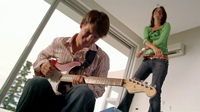 中景:年轻男子在卧室弹吉他/年轻女子在床上跳着舞/南非视频素材