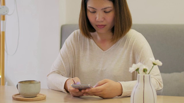 咖啡馆里，一位女士在喝咖啡时，在木桌上触摸智能手机视频下载
