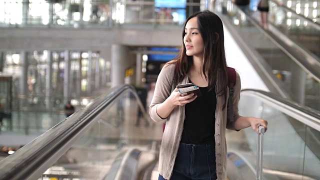 一名亚洲年轻女子在机场玩智能手机视频素材