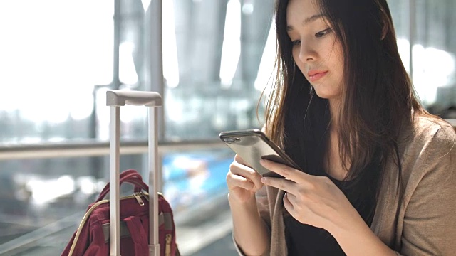 亚洲女性在等待航班时使用智能手机视频下载