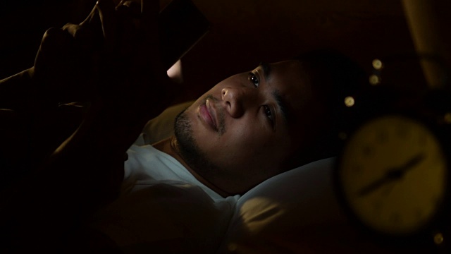 一名年轻人晚上在床上使用智能手机的视频视频素材