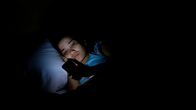 亚洲女人晚上在床上用智能手机视频下载