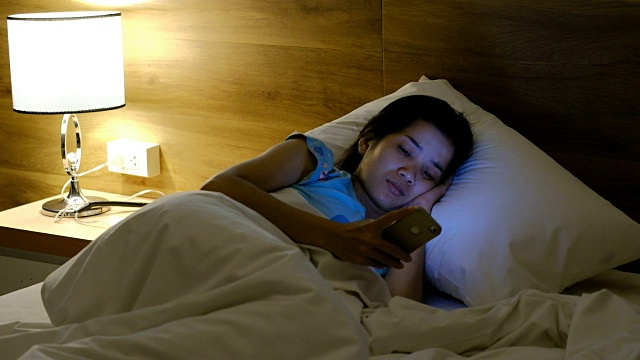 亚洲女人晚上在床上用智能手机视频素材