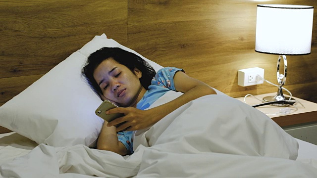 亚洲女人晚上在床上用智能手机视频素材