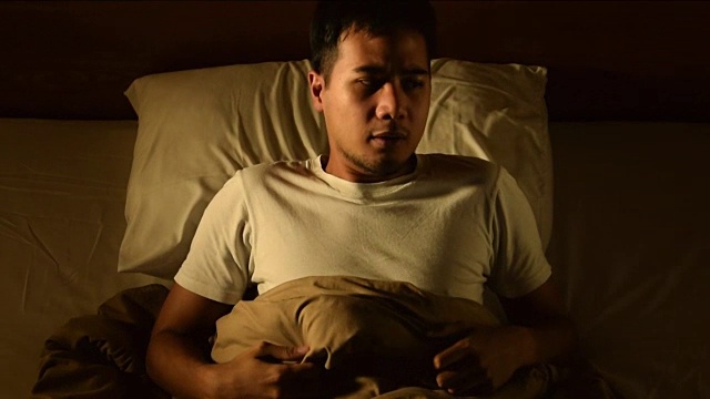 倾斜的镜头，一个年轻人在床上遭受失眠。噩梦的问题视频下载