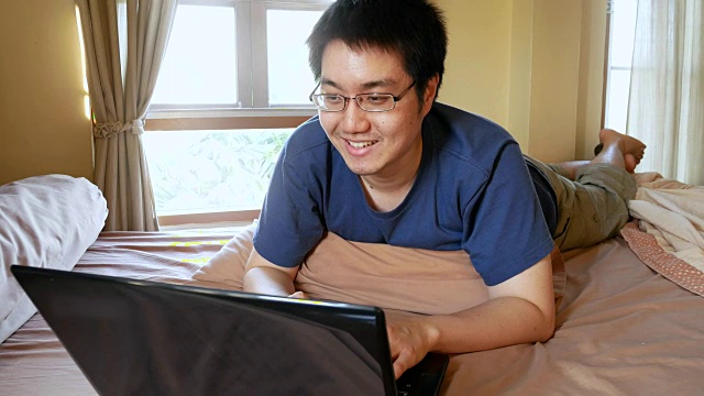 快乐的男人戴着眼镜用笔记本电脑在床上聊天聊天-家庭室内场景视频素材