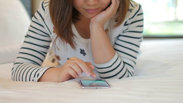 年轻女子在卧室的床上使用智能手机视频下载