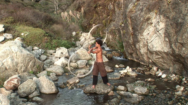 赤裸上身的男子站在溪流中间的岩石上，同时旋转多个大圆环/大苏尔，加利福尼亚视频素材
