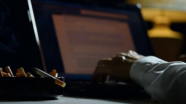 画面中，一名男子用手指夹着点燃的香烟，在用笔记本电脑工作视频下载