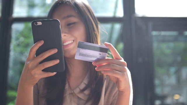 年轻的亚洲女人用信用卡在手机上购物视频素材