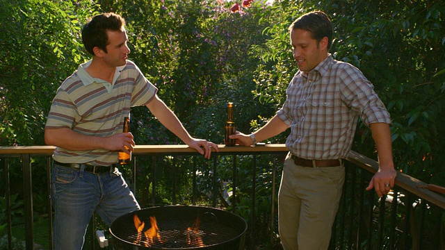 美国加州洛杉矶，两名男子在燃烧的烧烤架旁边聊边喝啤酒视频素材