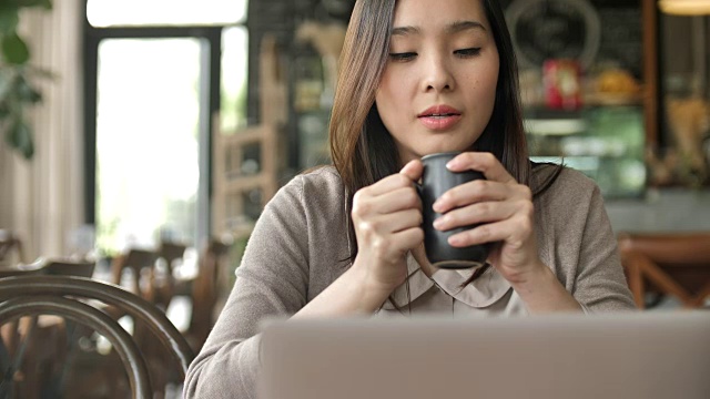 年轻女子看笔记本电脑和微笑与咖啡杯视频下载
