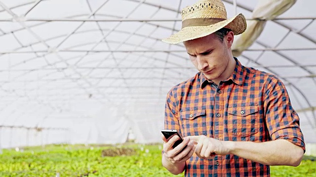 年轻的园丁在温室里使用智能手机视频下载